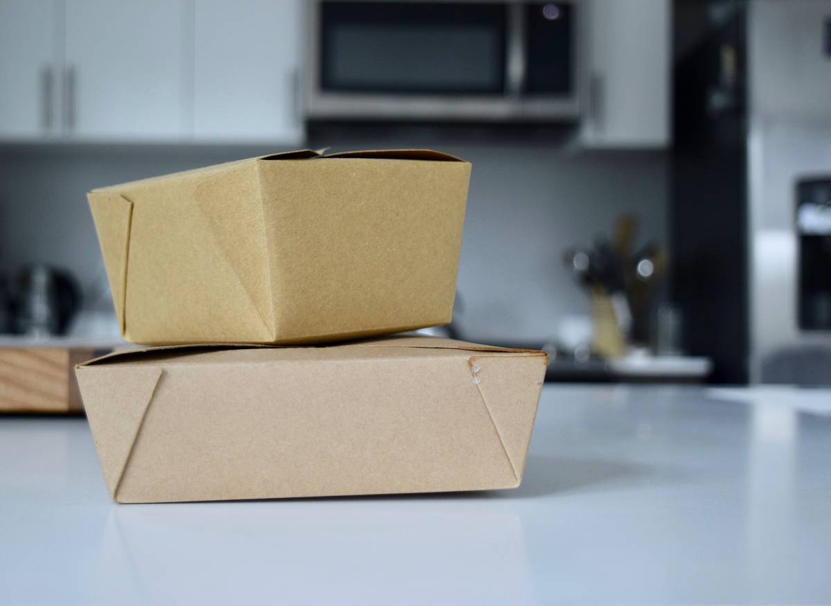 Stack of compostable food containers labeled biodegradable packaging for foods beside fresh produce